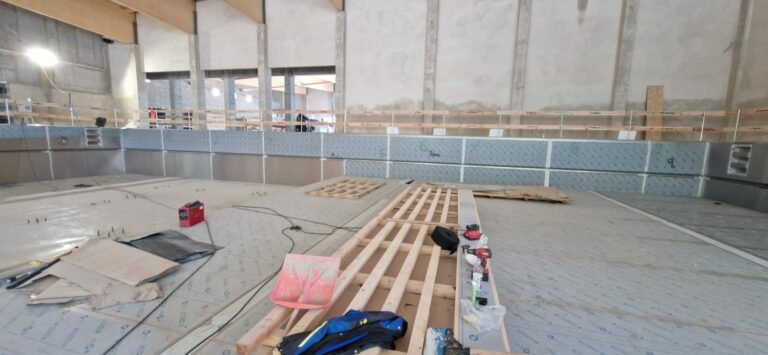 Indoor construction site with unfinished pool, wooden beams, and scattered tools.