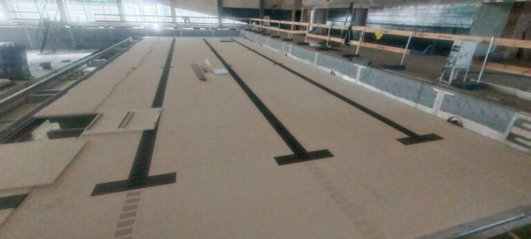 Indoor swimming pool under construction with tiled floor and wooden railings.