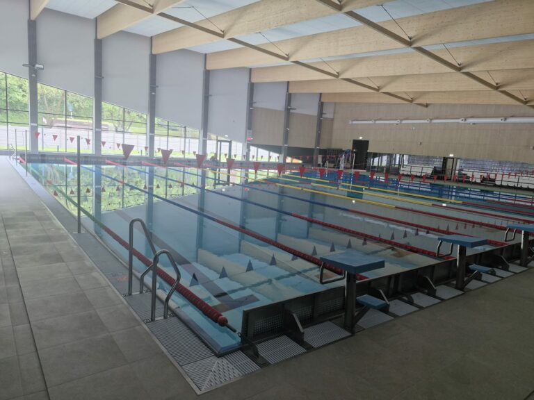Indoor swimming pool with lanes, diving boards, and large windows overlooking greenery.